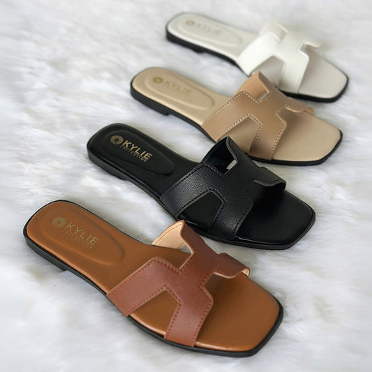 Top down view of Kylie Collection ladies flat sandals featuring H-shaped straps in dark tan, black, beige, and white colors arranged diagonally in Sri Lanka