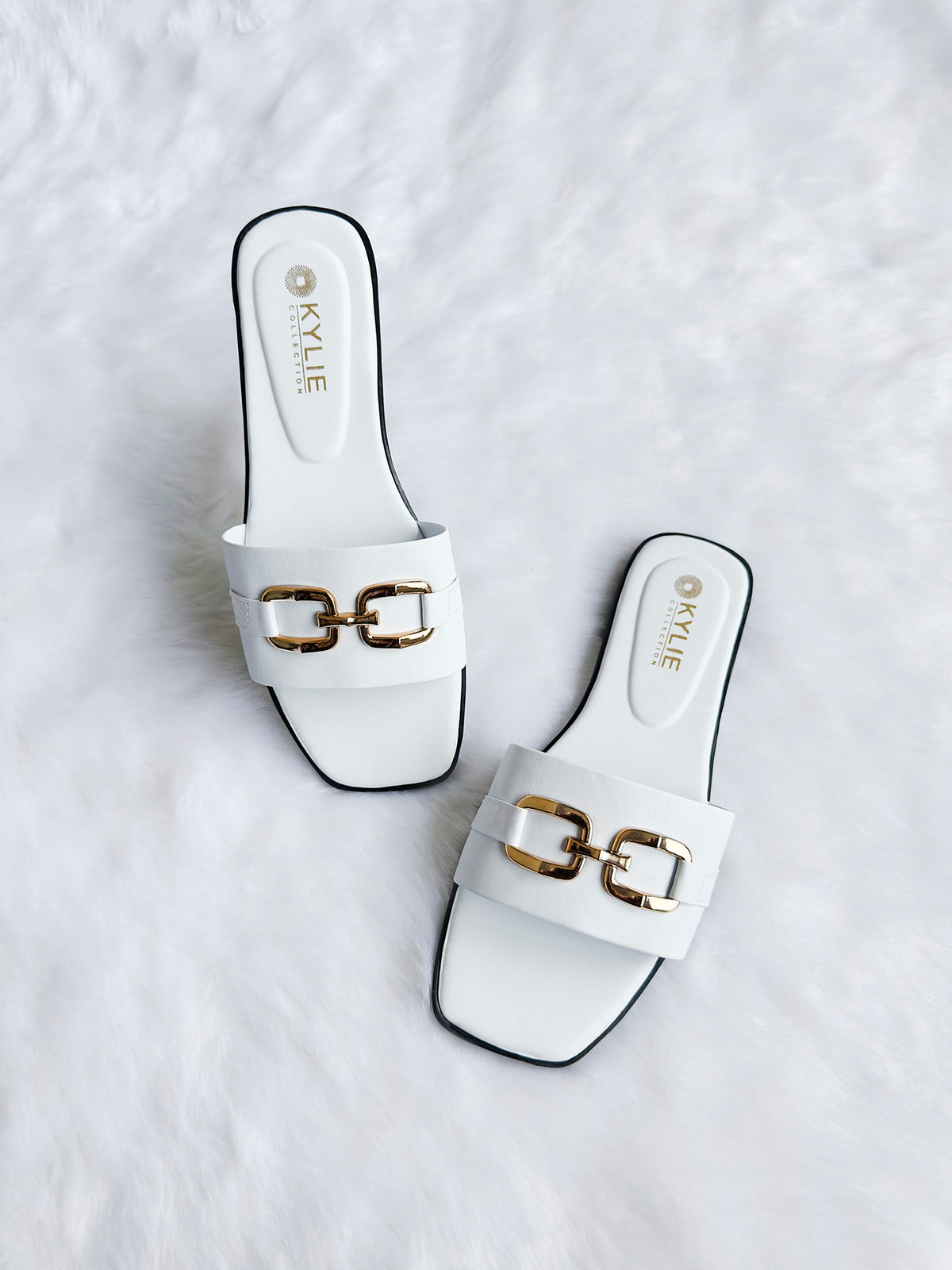 Top down view of Kylie Collection ladies white flat sandals featuring a wide strap with a gold link buckle detail in Sri Lanka