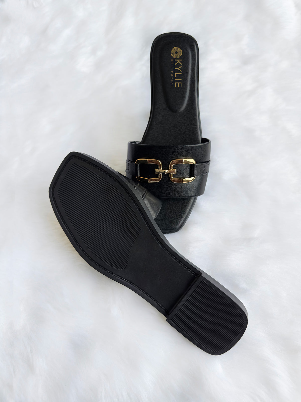 Top down view of Kylie Collection ladies black flat sandals featuring a wide strap with a gold link buckle detail and textured sole in Sri Lanka