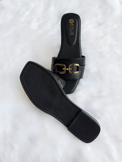 Top down view of Kylie Collection ladies black flat sandals featuring a wide strap with a gold link buckle detail and textured sole in Sri Lanka