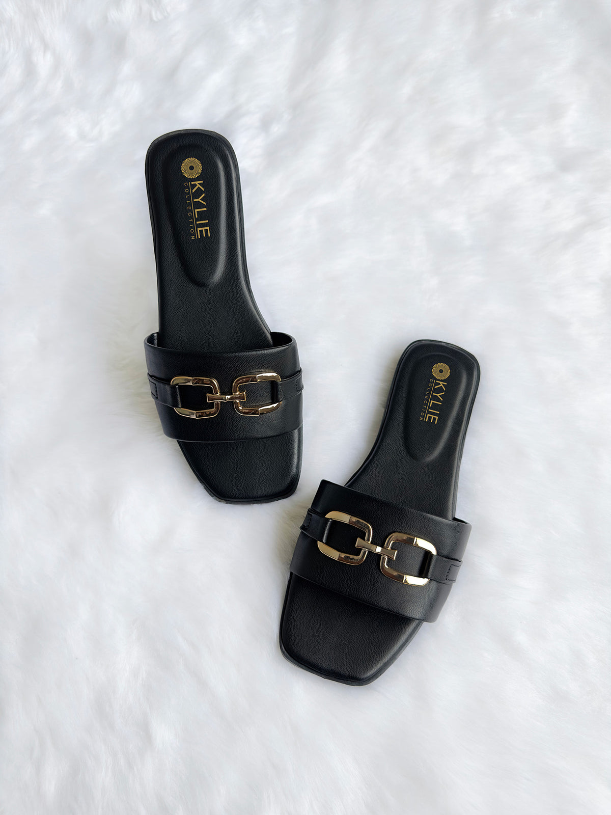 Top down view of Kylie Collection ladies black flat sandals featuring a wide strap with a gold link buckle detail in Sri Lanka