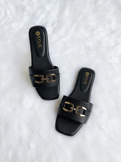 Top down view of Kylie Collection ladies black flat sandals featuring a wide strap with a gold link buckle detail in Sri Lanka