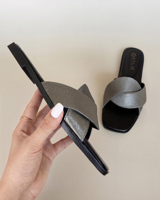 Close up of Kylie Collection ladies metallic silver slip-on flat sandals shown on hand in side profile with wide cross straps and a black sole in Sri Lanka